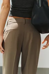Pantalón de tiro bajo color marrón, con bolsillos frontales, falsos bolsillos traseros de vivo y cierre delantero con cremallera y gancho metálico.