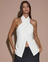 Top blanco sin mangas con cuello halter cruzado, espalda descubierta y abertura frontal.