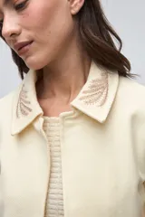 Chaqueta de lana fina sin teñir, con cuello clásico y bolsillos frontales. Presenta detalles bordados en el cuello y en los puños de las mangas. Es una prenda forrada con diseño exclusivo.