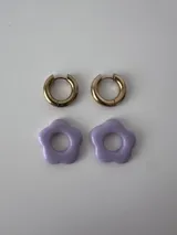 Aros de acero quirúrgico dorados con argollas pequeñas y dijes colgantes en forma de flor color celeste.