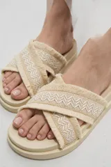 Sandalias planas color crudo con tiras cruzadas de tejido textil con diseño geométrico y detalles de flecos en los bordes.