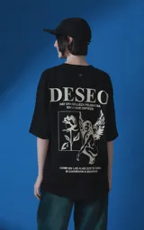 Remera de manga corta y cuello redondo con calce oversize. Presenta una estampa frontal en color crema con diseño artístico de un ángel y una rosa, acompañada de frases en español. Confeccionada en algodón premium.