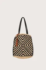 Bolsa tote de rafia tejida con patrón geométrico en negro y color natural, asas superiores de cuero negro y etiqueta colgante en tono tostado.