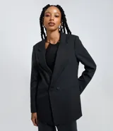 Blazer largo de mujer, color gris oscuro, con rayas verticales finas (riscas de giz). Presenta solapa de muesca, cierre frontal de dos botones y bolsillos de ojal.