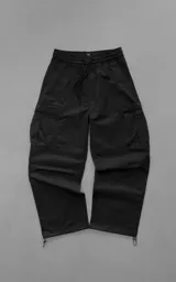 Pantalón cargo negro de corte regular y estilo urbano, confeccionado en textil técnico pesado. Cuenta con cintura elástica con cordón ajustable, múltiples bolsillos incluyendo amplios bolsillos cargo laterales, y puños ajustables con tancas en los tobillos.