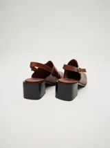 Zuecos de cuero vacuno con acabado en charol, color beige. Presentan un diseño clásico con taco cuadrado de madera de 5 cm y correa trasera ajustable con hebilla metálica.