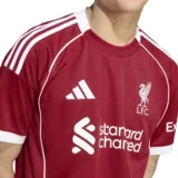 Camiseta de fútbol Adidas del Liverpool FC, modelo Home 25/26. Diseño rojo con detalles blancos en cuello, mangas y hombros. Incluye logo de Adidas, escudo del club y sponsor Standard Chartered en el frente.