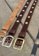 Cinto de cuero marrón con tachas metálicas plateadas y hebilla rectangular plateada.