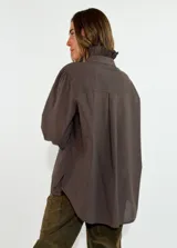 Camisa de algodón color blanco, con cuello redondo y detalle de volados en el cuello y puños. Presenta mangas largas con puños elásticos y un diseño de corte holgado con ruedo asimétrico, más largo en la parte trasera.