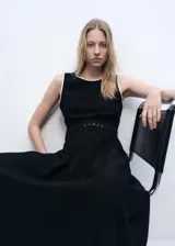 Vestido midi negro sin mangas, con cuello redondo, cinturón con hebilla y falda evasé con pliegues. Presenta cierre lateral con cremallera y botón en la parte posterior.