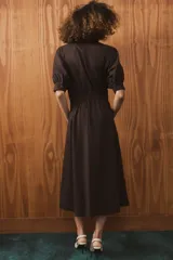 Vestido midi de algodón con cuello solapa, cierre frontal con botones y mangas cortas abullonadas con puños. Presenta un diseño evasé con bolsillos laterales ocultos y elástico en la espalda.
