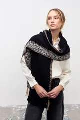 Bufanda de gran tamaño tejida en color negro, con detalles de guardas geométricas en tonos beige y blanco en los bordes y terminación con flecos.