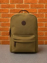 Mochila de lona color verde militar, con compartimento principal con cierre, bolsillo frontal con cierre y detalles en cuero marrón. Incluye manija superior y logo circular grabado en el frente.