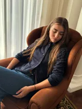 Blazer de jean azul con cuello, solapa y cuatro botones frontales. Presenta volados de encaje negro en cuello y delantero, mangas largas con pliegues y bolsillos plaqué. Interior con terminación en hilo bordó.