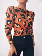 Remera manga larga color naranja con estampado animal print negro y dorado, con nudo en la parte delantera.
