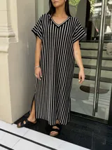 Vestido largo de tejido de punto con diseño de rayas verticales en blanco y negro. Presenta escote en V, mangas cortas y tajos laterales en el ruedo para mayor movimiento.