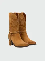 Botas estilo western de gamuza color marrón, con bordados decorativos en la caña y detalle de flecos laterales. Presentan un diseño de punta fina y taco cuadrado, con costuras detalladas en la puntera.