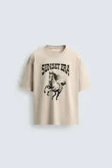 Camiseta de corte relaxed fit, color beige claro con efecto lavado, cuello redondo y manga corta. Estampado frontal en negro con texto "SUNSET ERA" y un caballo galopando.