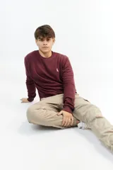 Buzo de punto color bordó, de corte clásico y manga larga. Presenta un pequeño logo bordado en el pecho.