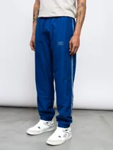 Pantalón deportivo azul de nylon con corte holgado, cintura elástica con cordón ajustable, bolsillos laterales y logo de Umbro bordado en el muslo.