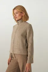 Campera de lana fina sin teñir, con cuello alto, cierre frontal completo y diseño de corte recto con pespuntes decorativos en puños, ruedo y cuello.