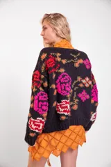 Cardigan de lana merino tejido y bordado a mano de calce holgado con cuello a la base, mangas largas y cierre frontal de botones. Presenta un diseño artesanal con bordados coloridos en las mangas y el cuerpo.