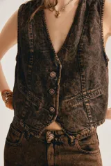 Chaleco de denim marrón con efecto acid wash, escote en V profundo, cierre frontal con botones metálicos y bolsillos ribeteados simulados.