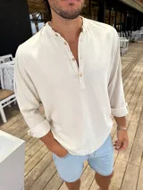 Camisola de lino color beige, con cuello mao y cierre frontal parcial con botones. Presenta mangas largas con puños doblados.