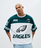 Remera de corte oversized con diseño deportivo de los Philadelphia Eagles. Presenta cuello redondo, mangas cortas con detalles de rayas y estampa frontal del equipo. Confeccionada en algodón.
