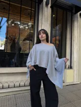 Poncho de hilo liviano en color gris, con diseño sin cuello y caída fluida. Presenta un corte asimétrico y una textura tejida, ideal para superponer sobre otras prendas.