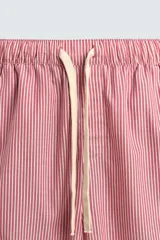 Pantalón de corte relajado confeccionado en popelín de algodón, con estampado de rayas verticales blancas sobre fondo rosado. Posee cintura elástica ajustable con cordón y bandas laterales lisas en color rosado oscuro, ribeteadas con un vivo blanco.