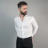 Camisa blanca de manga larga, 100% algodón, con cuello clásico y botones frontales. Presenta un pequeño logo bordado en el pecho.