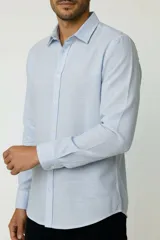 Camisa de algodón celeste claro, de corte holgado, con mangas largas, cuello camisero y cierre frontal con botones.