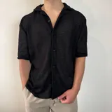 Camisa de manga corta con textura calada y tejido abierto, color negro, con cuello solapa y cierre frontal de botones.