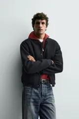 Chaqueta relaxed fit de color negro, confeccionada en tejido de canalé con mezcla de lana. Presenta cuello redondo, puños y dobladillo en rib elástico, bolsillos frontales de vivo y cierre con botones a presión.