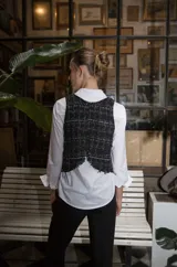 Chaleco de corte recto y cuello a la base, confeccionado en tejido de tweed con textura en tonos negro y blanco. Presenta un diseño sin mangas con terminaciones deshilachadas y cierre posterior.
