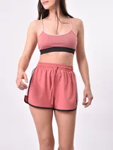 Short deportivo rosado con cintura elástica con cordón de ajuste, ribetes negros y franja lateral en color rosa claro.
