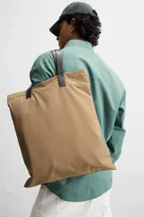 Bolso tipo shopper color beige, fabricado en tejido técnico con asas de mano de piel color negro. Tiene compartimento principal con cierre de imán y bolsillo interior con cremallera.