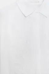 Camisa de corte fluido con cuello solapa y manga larga con puños. Presenta detalles de bordados a tono en el frente y cierre frontal con botones ocultos bajo solapa.