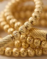 Pulsera esclava de acero con baño de oro, compuesta por pequeñas esferas texturizadas y un detalle central cilíndrico estriado.