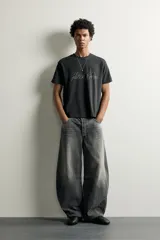 Jeans de denim de algodón color gris con efecto lavado, de corte relaxed barrel fit y tiro medio. Presenta diseño amplio con pinzas en las rodillas y costuras curvas, cierre frontal con botones y cinco bolsillos tradicionales.