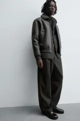 Cazadora oversize de efecto piel color negro, con interior y cuello solapa de pelo sintético gris a contraste. Cuenta con bolsillos de vivo en la cadera, acabados en rib elástico y cierre frontal con cremallera.