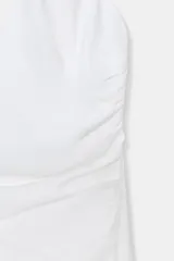 Vestido midi blanco con cuello halter, escote pico, detalle de frunces en el delantero y abertura. Cierre en espalda con cremallera oculta y botones.