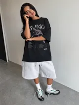Remera marrón oversize con efecto acid wash, corte amplio y mangas cortas. Presenta un estampado frontal en tonos celestes y grises con la inscripción 'Sumo', una ilustración de un luchador de sumo y detalles tipográficos alusivos a un álbum musical.
