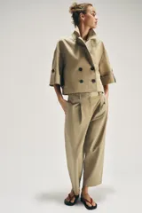 Trench corto de color beige, con cuello de solapa, cierre cruzado con botones y mangas cortas con vuelta y trabilla con botón.