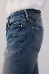Jeans de cinco bolsillos en denim de algodón rígido, color azul medio con efecto desgastado y lavado. Modelo de cintura clásica con cierre de botón y corte relajado de cadera a bajo con pierna recta más amplia.