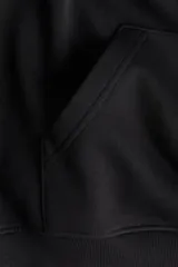 Buzo negro con capucha de doble capa, hombros caídos, bolsillo canguro frontal y puños y bajo acanalados. Interior cepillado suave.