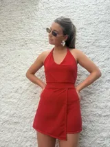 Mono corto color rojo con escote halter y espalda descubierta. Presenta corte a la cintura y falda cruzada tipo pareo.