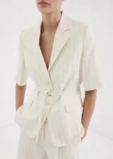 Blazer corto de mezcla de lino en color beige con rayas sutiles, de corte recto, cuello con solapa de muesca, mangas tres cuartos, cierre frontal de un botón y bolsillos con solapa.