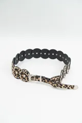 Cinturón de estilo western con diseño de animal print, compuesto por piezas circulares unidas, decoradas con tachas metálicas plateadas. Cuenta con hebilla y puntera metálicas grabadas.